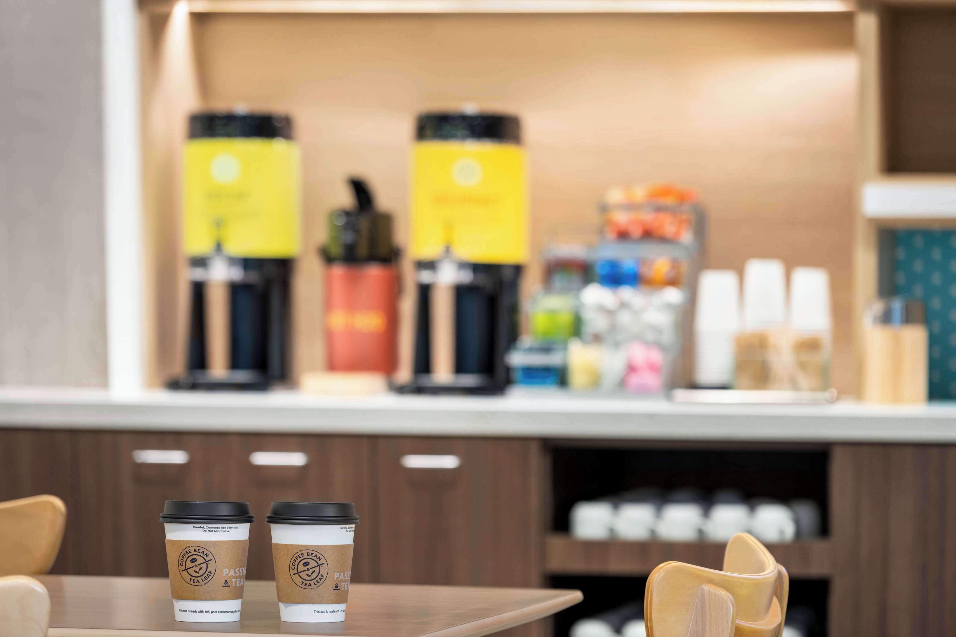 Un café avec deux tasses de café posées sur une table, une machine à café, et divers types de grains de café et de produits en arrière-plan.