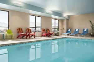 Zona de piscina con varias sillas de descanso y una mesa, ventanas amplias y vistas a las montañas.