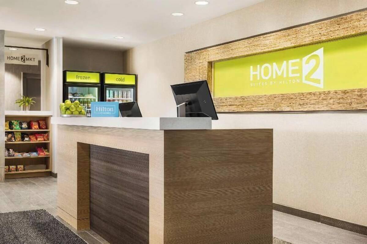 Een hotel receptiebalie met een 'HOME 2 Suites by Hilton' bord, een 'Hilton' bord, en een bord met de tekst 'bevroren' en 'koud'.