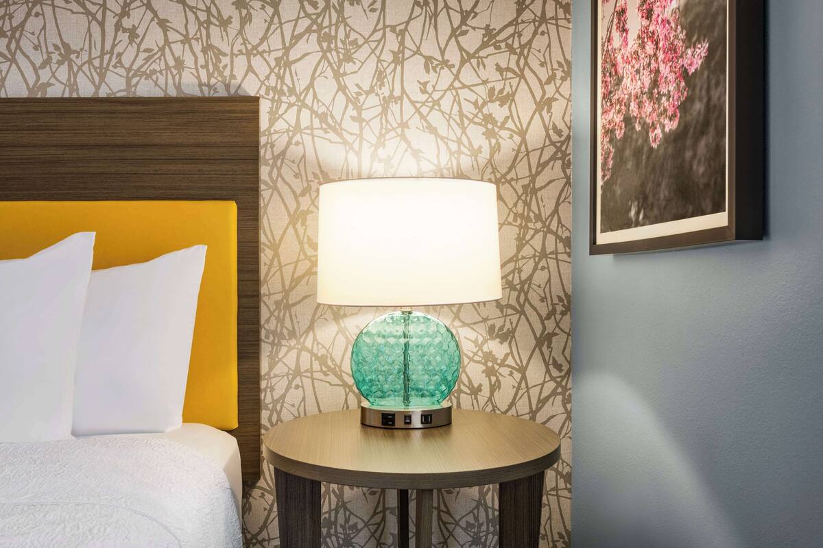 Een hotelkamer met een bed, een ronde tafel met een lamp en een behang met bloemen.