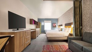 Een moderne hotelkamer met een bed, een sofa, een bureau met een flatscreen televisie en een kamerbreed tapijt met een patroon.