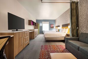 Habitación de hotel moderna con cama, sofá, escritorio y televisor de pantalla plana, además de un tapete estampado.