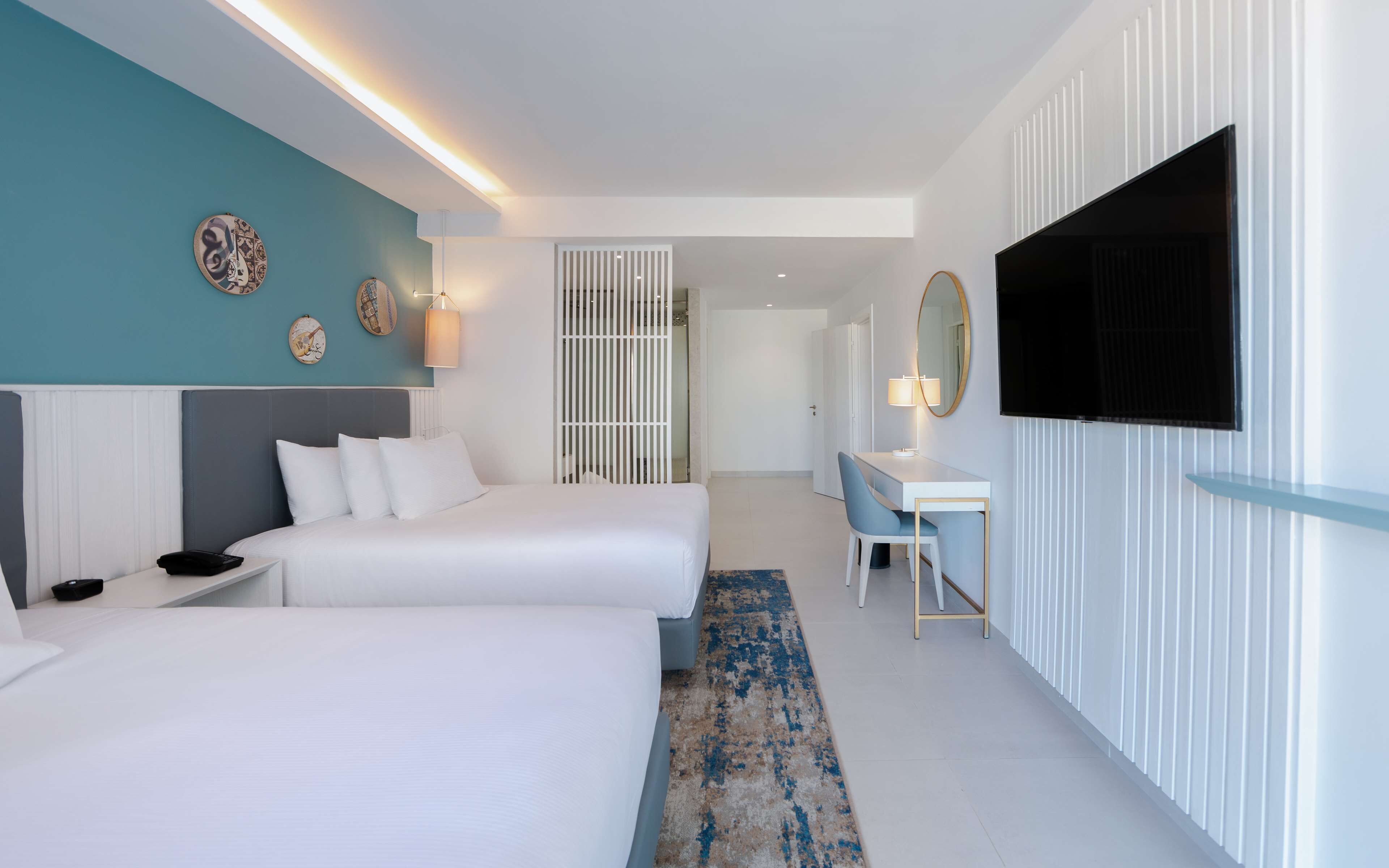 Una habitación de hotel moderna con dos camas, un escritorio, un televisor y detalles decorativos en la pared.