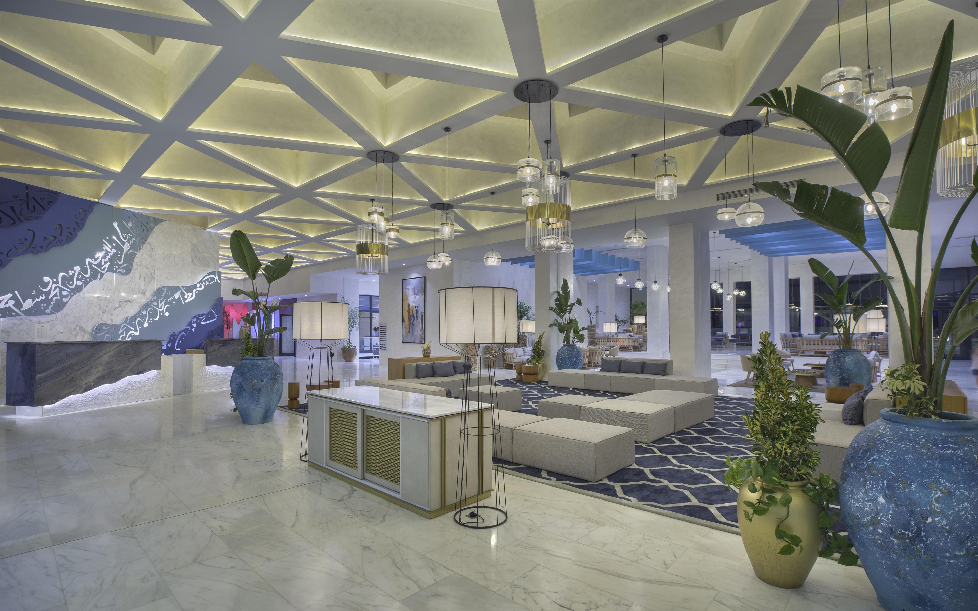 A modern lobby with a high ceiling, geometric ceiling design, and multiple hanging pendant lights.