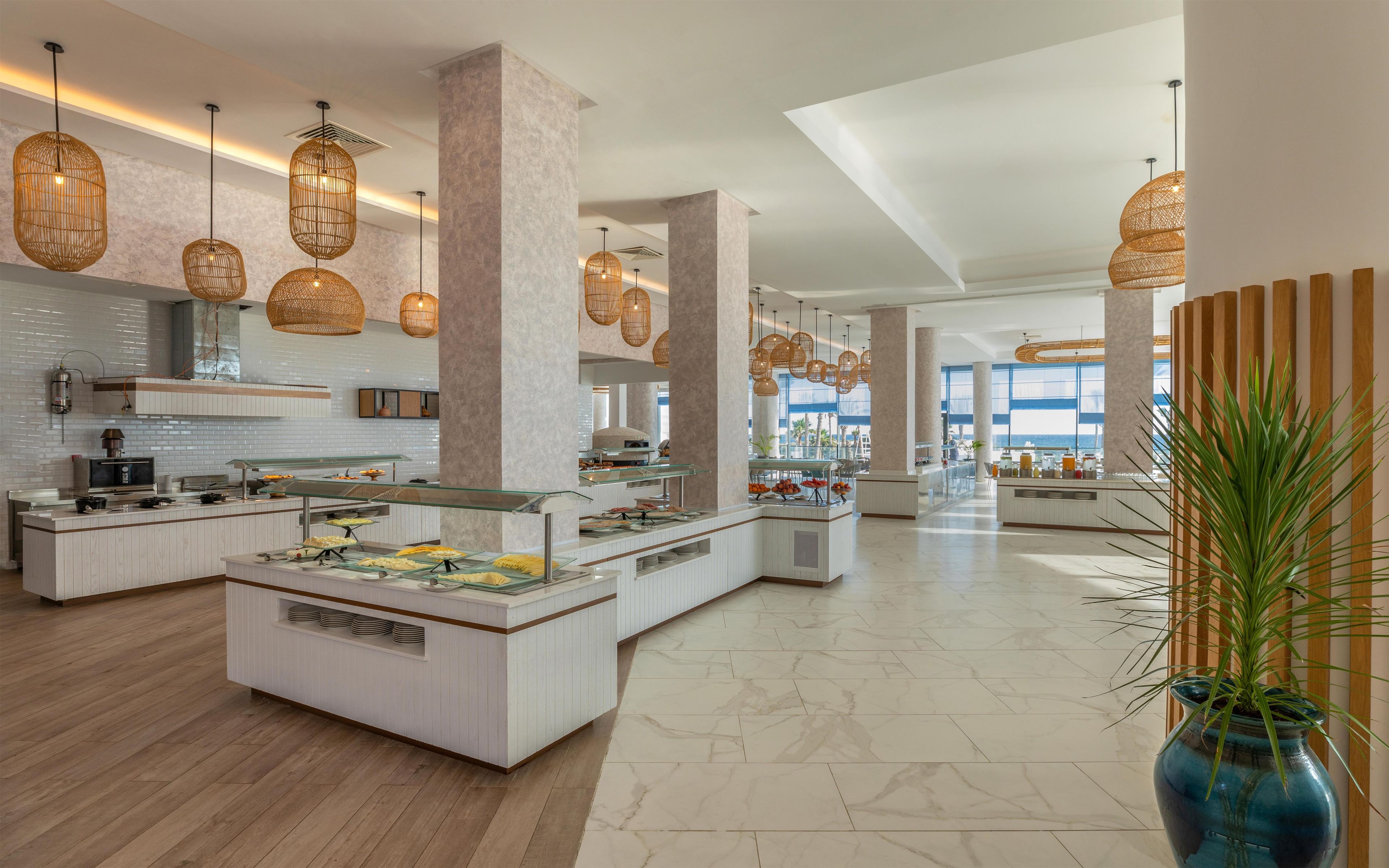 A modern hotel lobby with a central island, buffet area, and large windows offering a view.