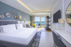 A modern hotel room with a large bed, a desk, a TV, and a balcony with a view of the sea. - Hilton Skanes Monastir Beach Resort (Monastir)