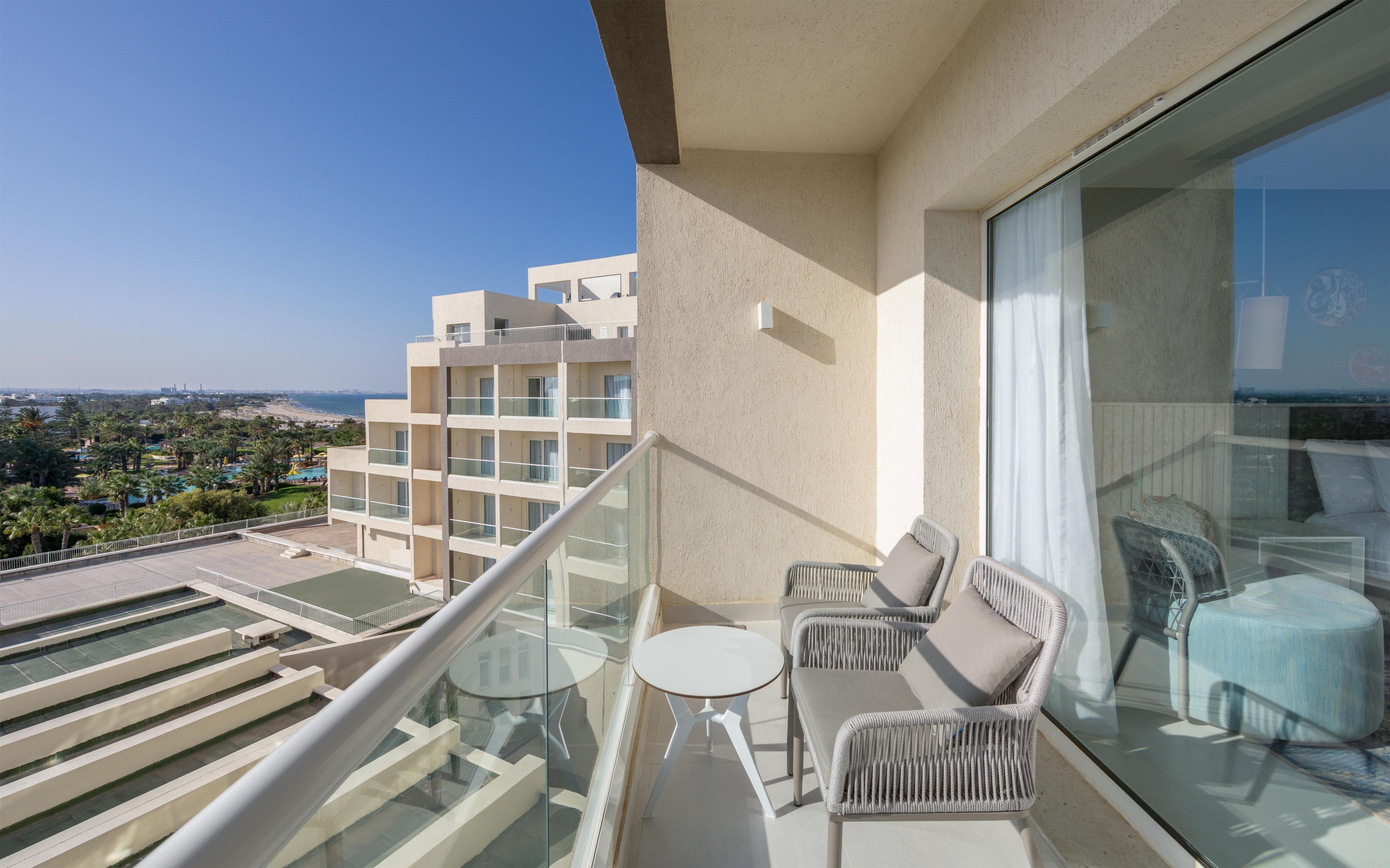 A balcony with a glass railing, a small table, and two wicker chairs.