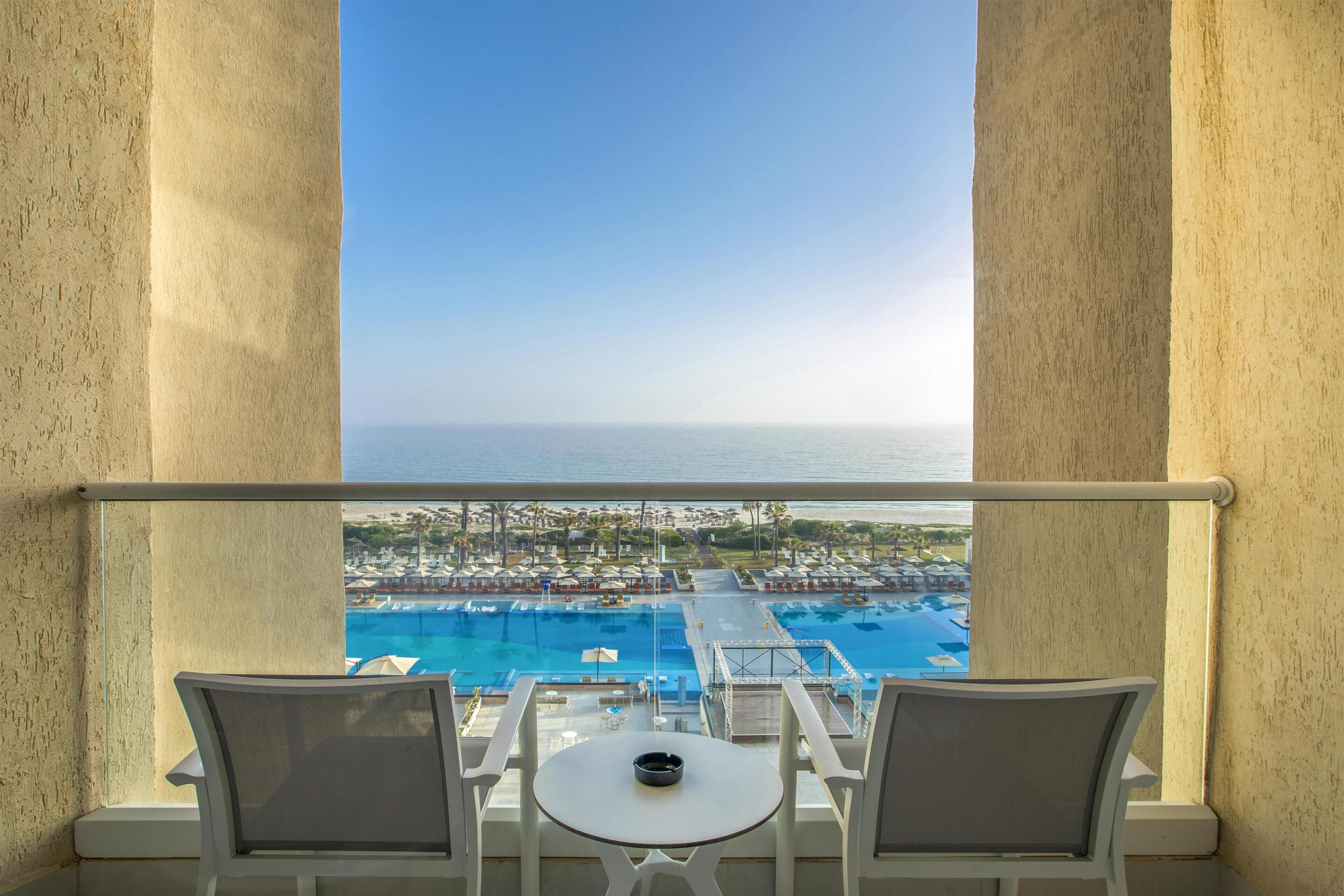 Ein Balkon mit zwei Stühlen und einem kleinen Tisch mit Blick auf einen Pool und das Resortgelände.