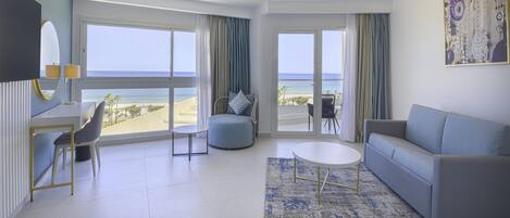 A modern hotel room with a large window, a sofa, a coffee table, and a desk with a chair.