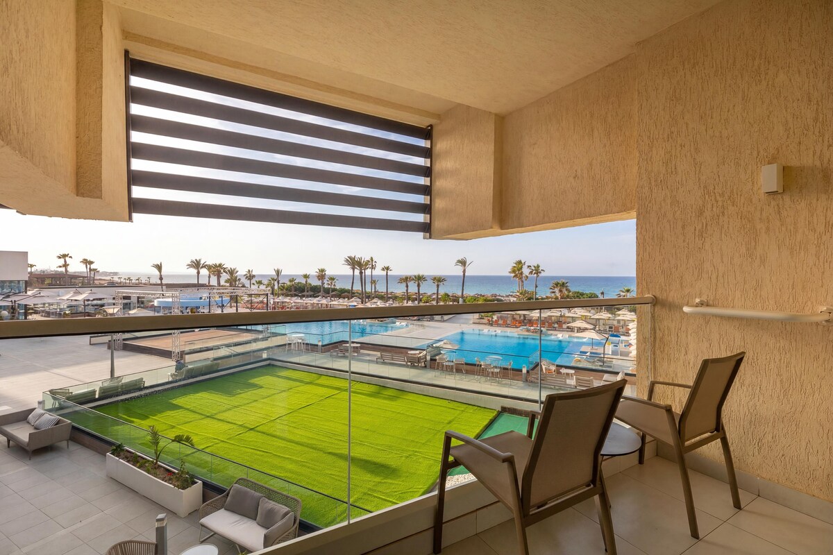 Un balcón con vistas a una piscina y una cancha de tenis, amueblado con sillas y una mesa.