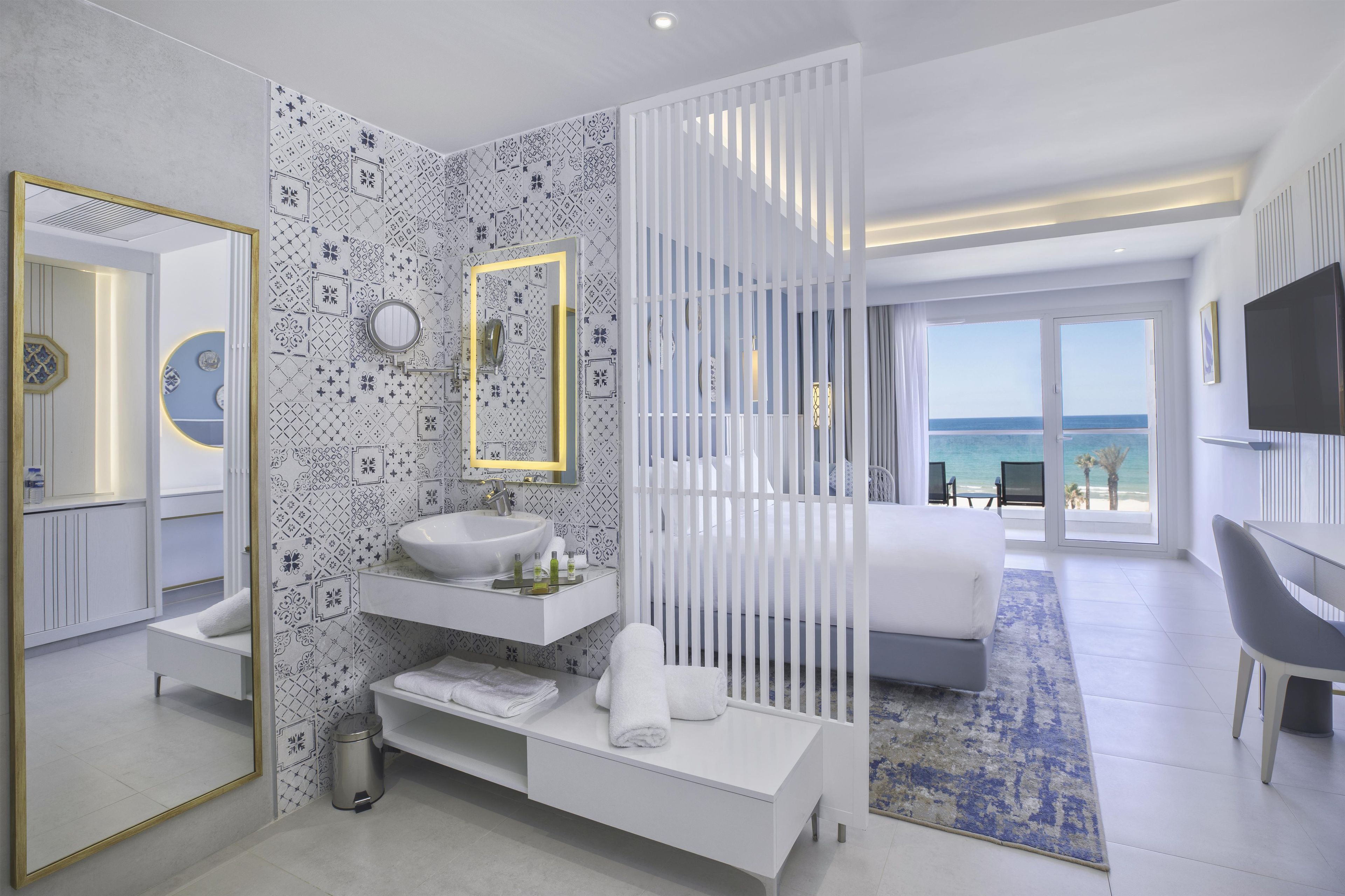 Un baño de hotel moderno con lavamanos, espejo y retrete.