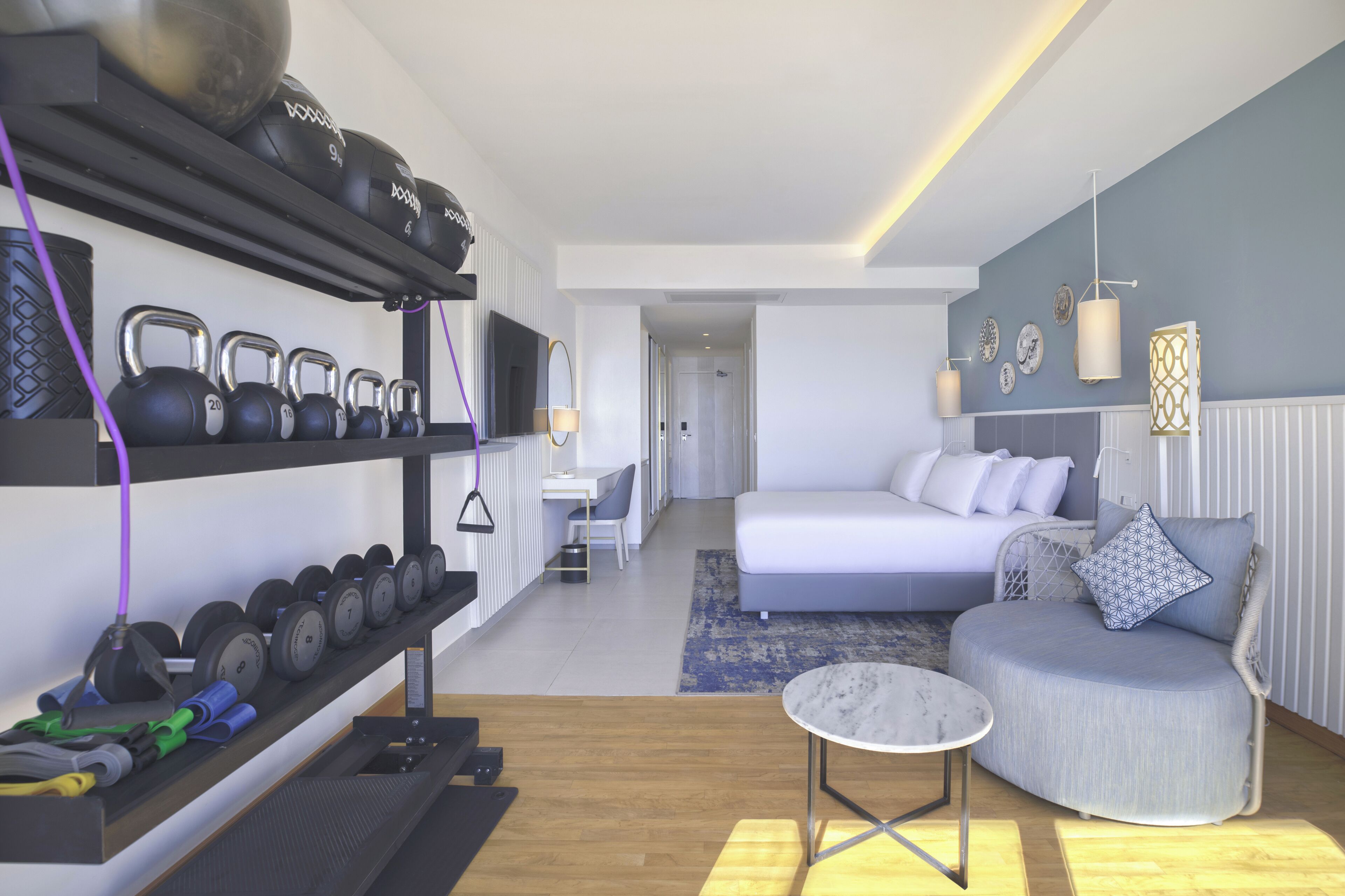 A modern hotel room with a gym area, a bed, and a small seating area.