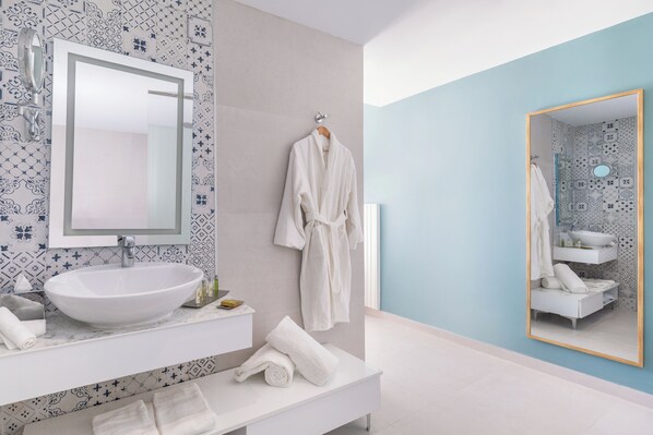 Un baño moderno con un lavamanos blanco grande, un espejo y una bata colgada en la pared.