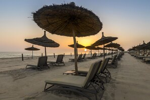 A beach with rows of sun loungers and thatched umbrellas, a clear sky, and the ocean in the background. - Hilton Skanes Monastir Beach Resort (Monastir)