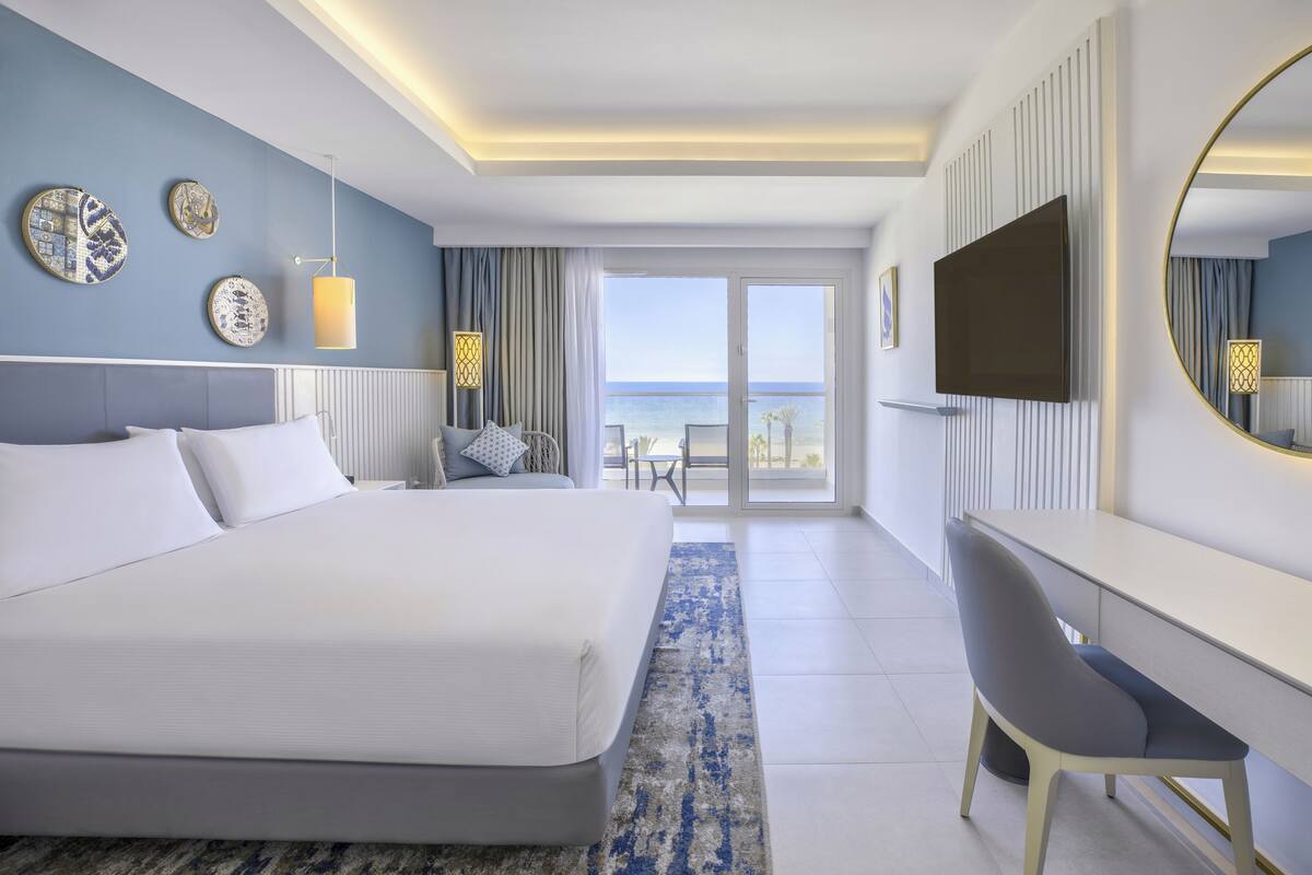 Una habitación de hotel moderna con una cama grande, un escritorio, un televisor y un balcón con vistas al mar.