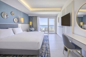 Una habitación de hotel moderna con una cama grande, un escritorio, un televisor y un balcón con vistas al mar.