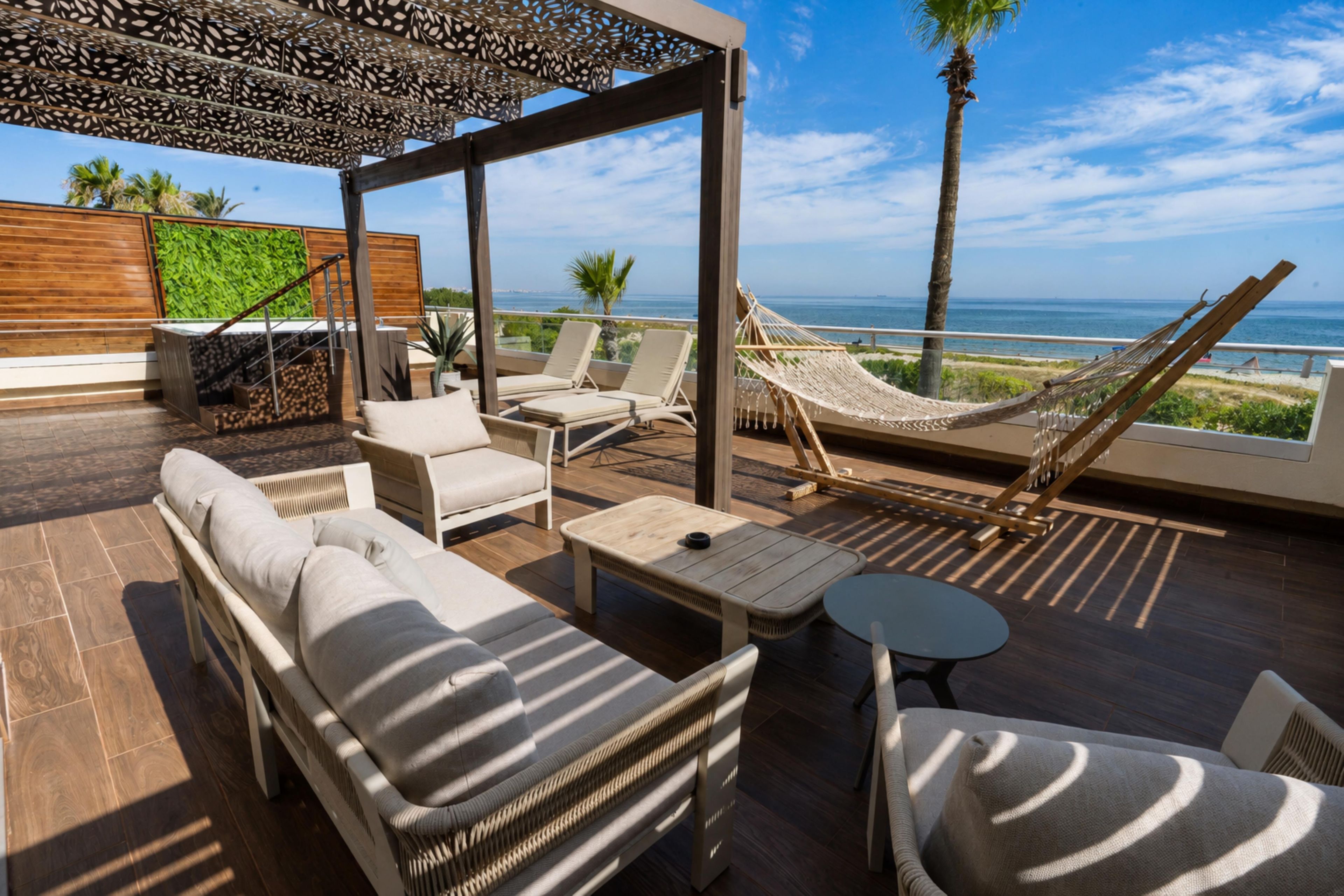 A sunlit outdoor lounge area with a hammock, lounge chairs, and a view of the sea.