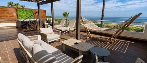 A sunlit outdoor lounge area with a hammock, lounge chairs, and a view of the sea.
