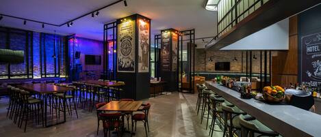 A modern bar area with high stools, a long counter, and a variety of bottles and glasses.