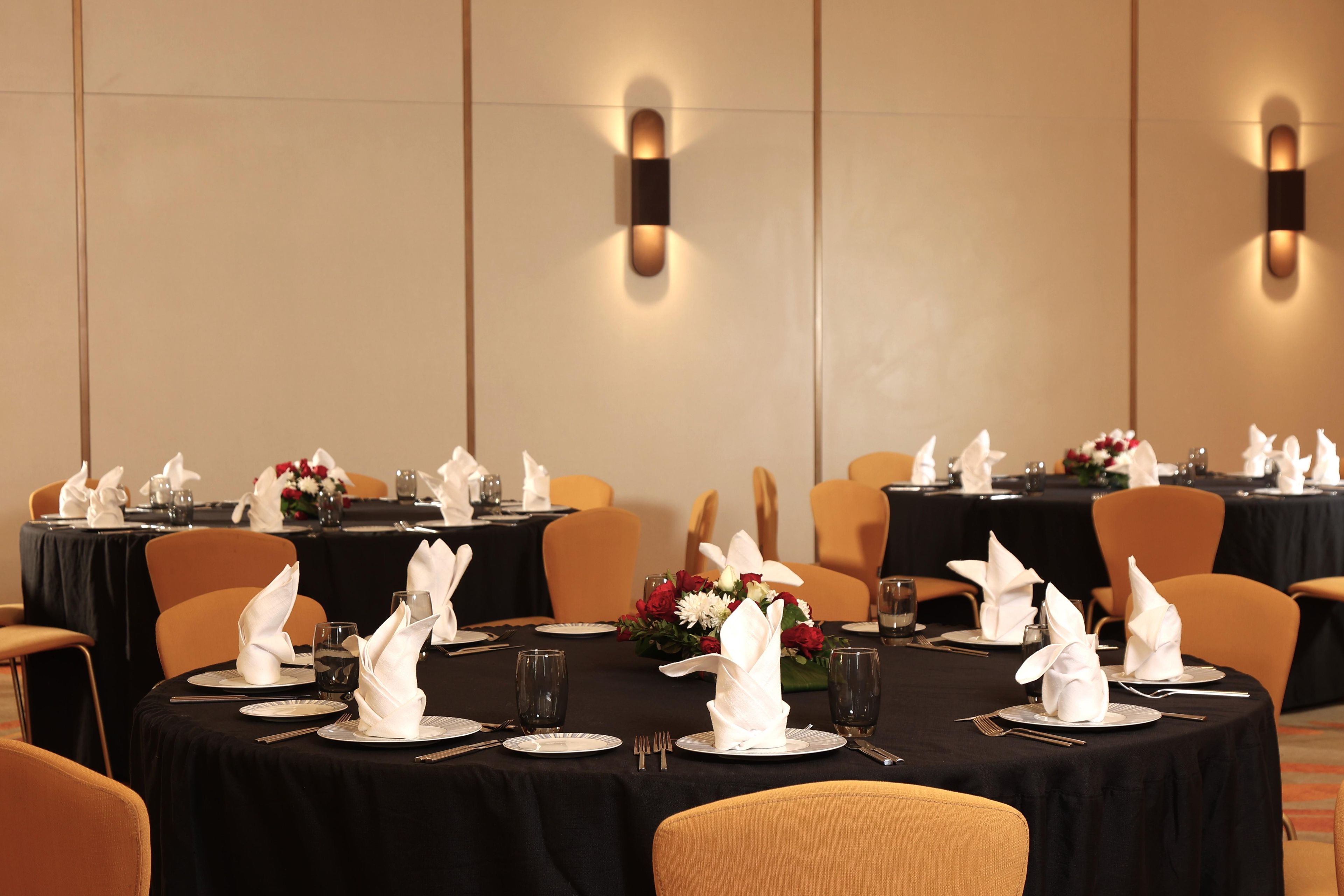 A conference room with round tables, each set with plates, cutlery, and folded napkins.