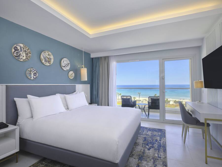 Ein modernes Hotelzimmer mit einem großen Bett, einem Schreibtisch und Blick auf den Strand.
