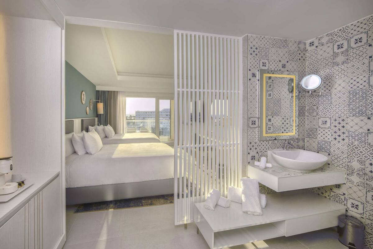 Una habitación de hotel moderna con una cama, un baño con un lavamanos grande y vistas a la ciudad a través de la ventana.