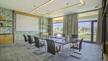 Un salón de conferencias con una gran mesa, sillas, una pizarra y vistas a palmeras y edificios a través de las ventanas.