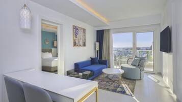 Une chambre d’hôtel moderne avec un lit, un canapé bleu, une table basse ronde et un téléviseur.