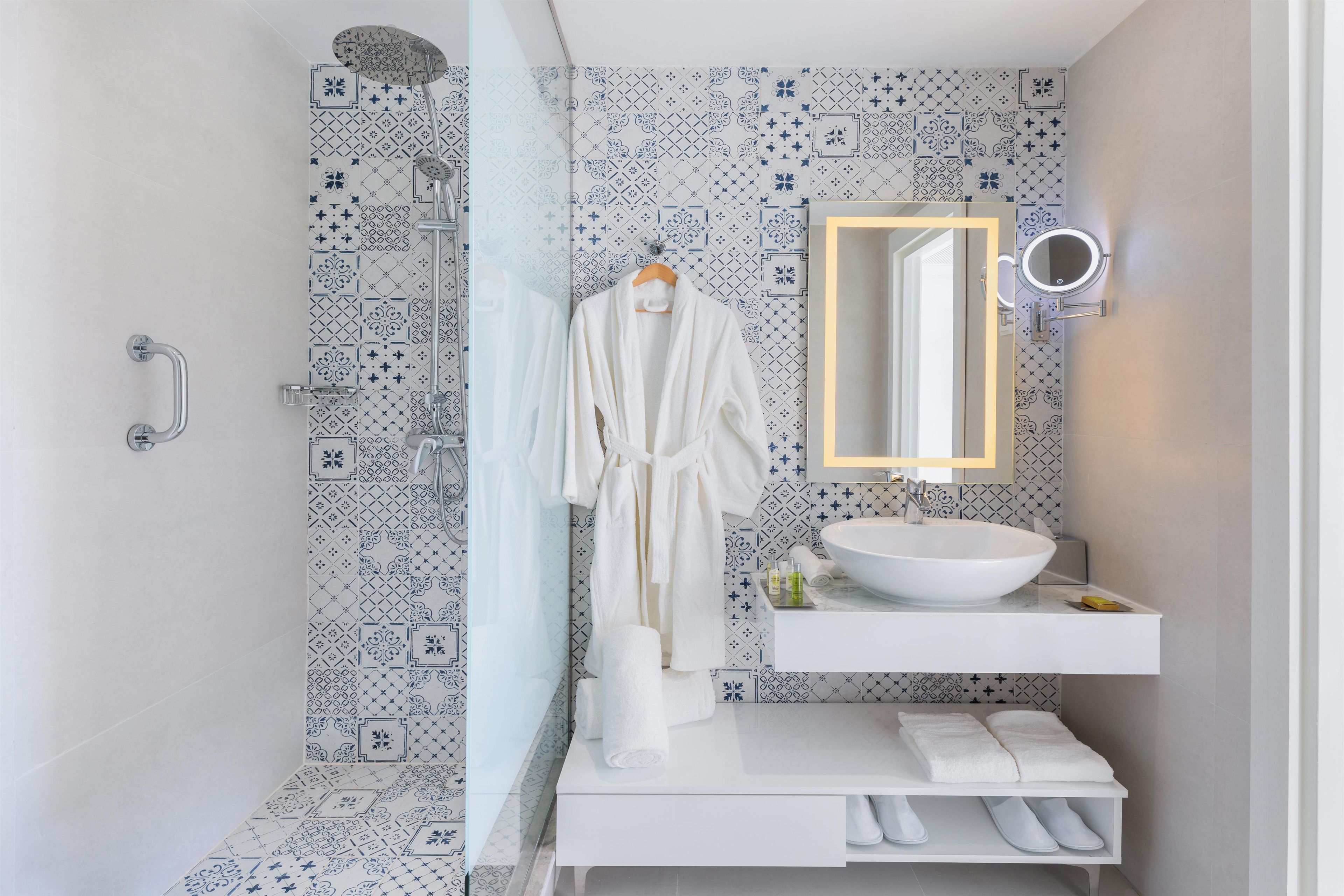 Baño con lavamanos blanco, espejo con luz y zona de ducha.