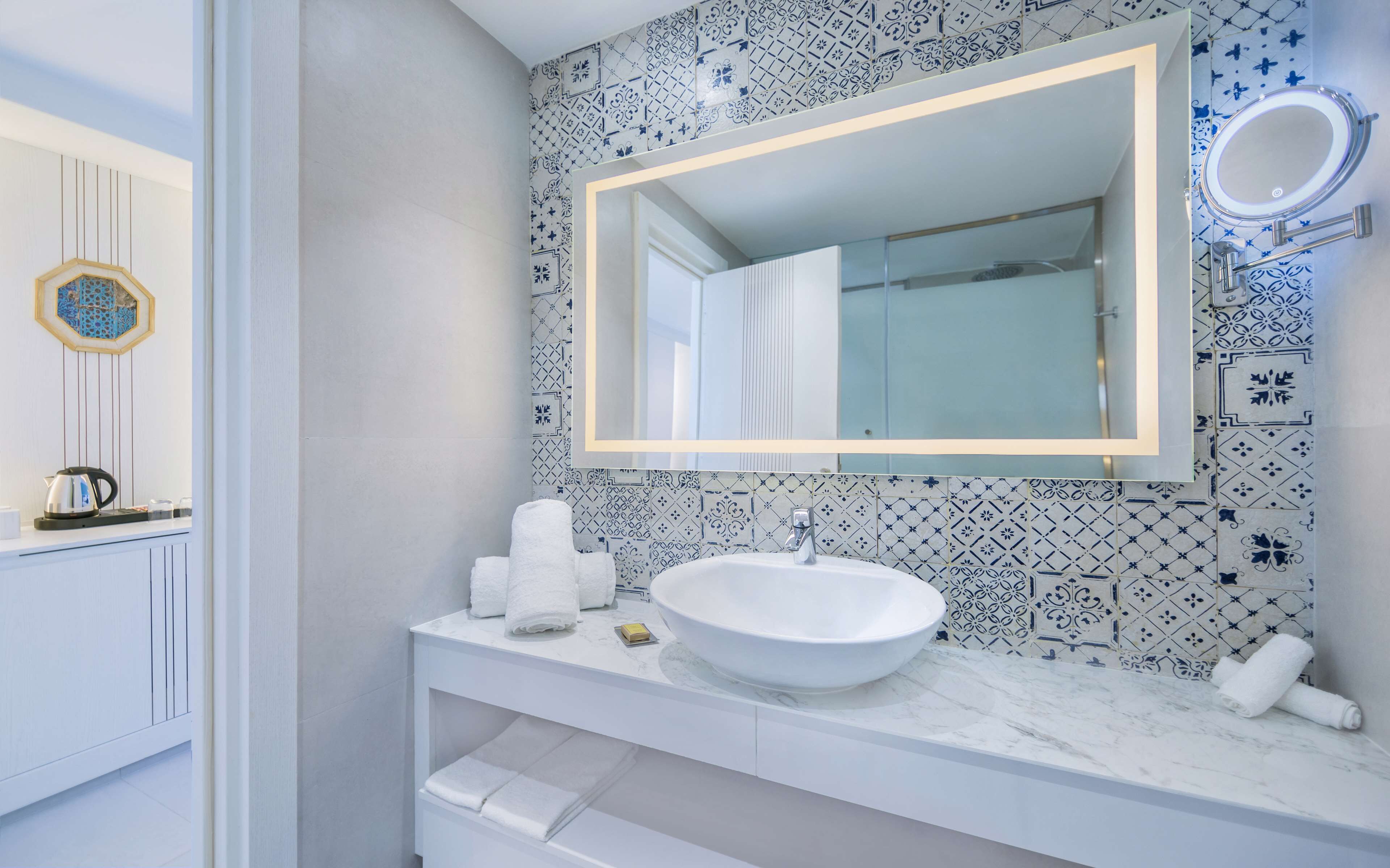 A modern bathroom with a white sink, a large mirror, and patterned tiles.