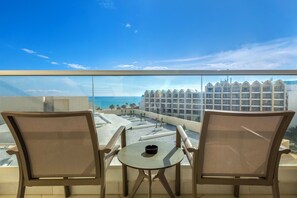 Un balcón con dos sillas y una mesita pequeña, con vista a una playa y un edificio de hotel.