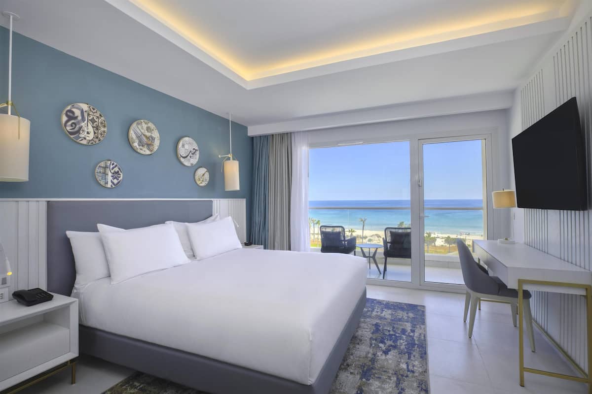 Habitación de hotel moderna con una cama grande, un escritorio y vista a la playa.