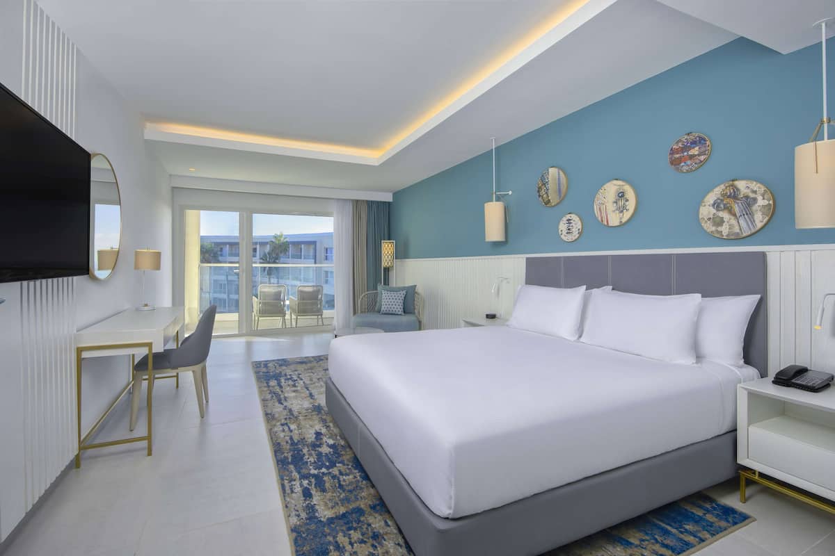 Una habitación de hotel moderna con una cama grande, un escritorio y un balcón con sillas.