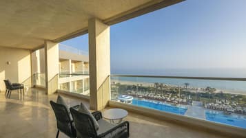 Un balcon avec vue sur une piscine et une plage, comprenant des chaises et une table.