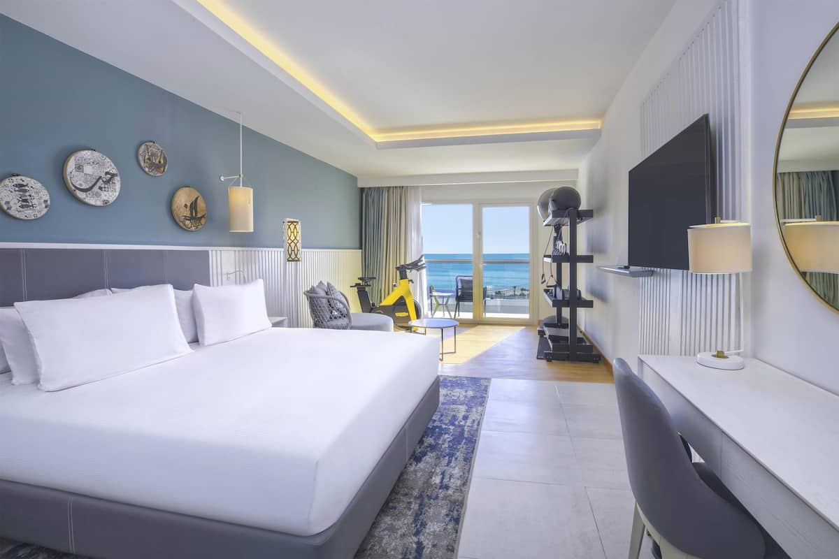 Habitación de hotel moderna con una cama grande, un escritorio, televisión y vista al mar.