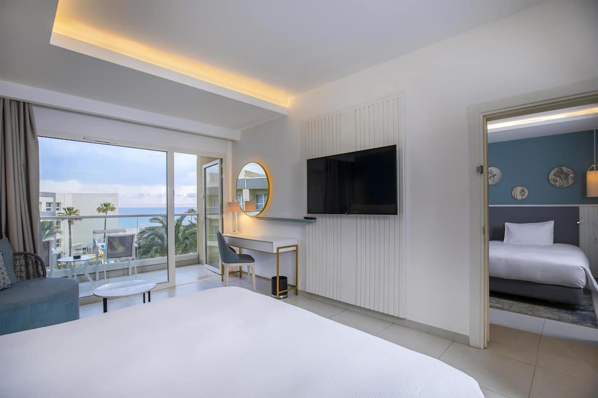 Habitación de hotel con una cama grande, un escritorio con silla, televisión y balcón con vistas.