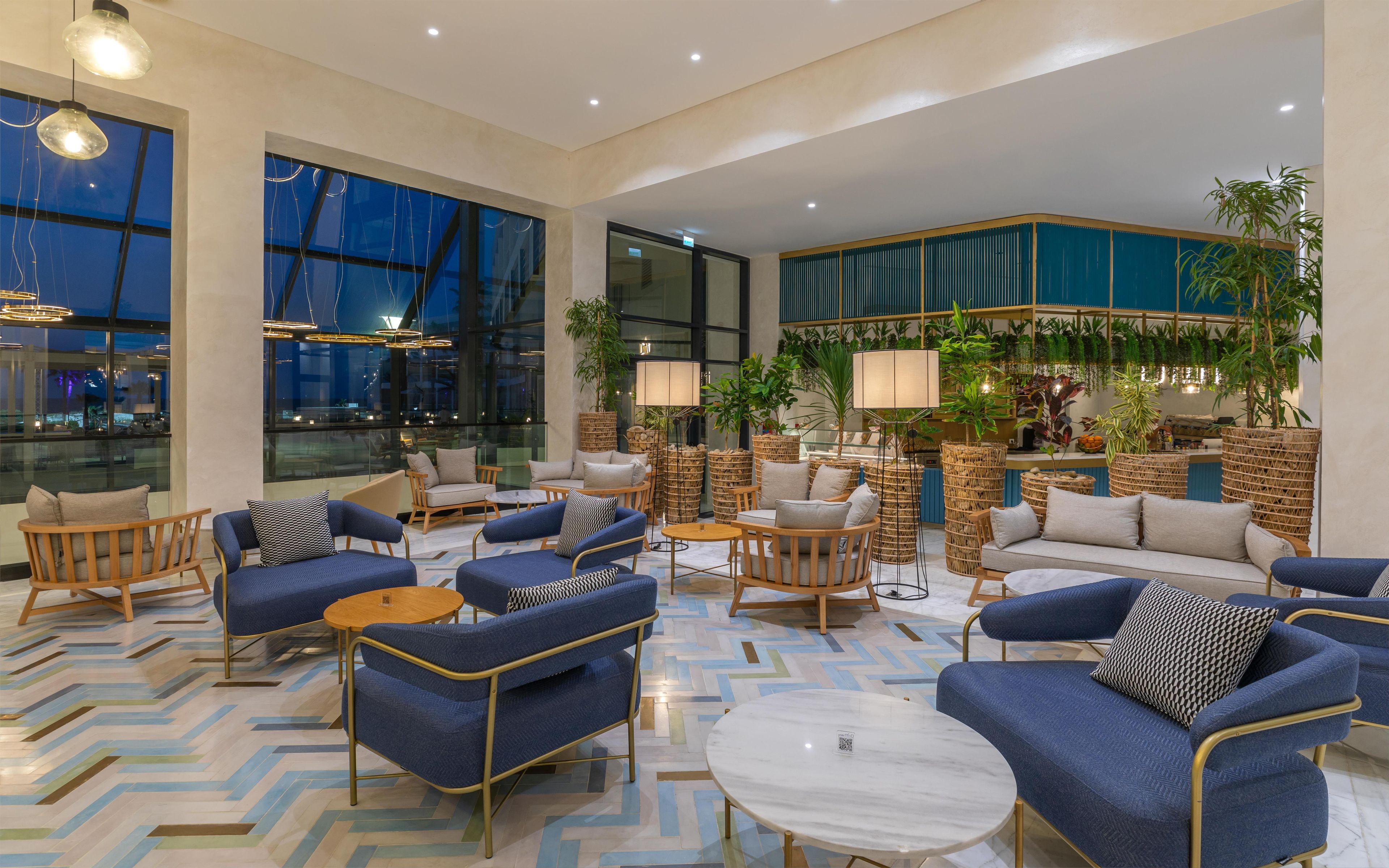 A spacious lobby with modern furniture, large windows, and indoor plants.