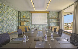 Une salle de conférence équipée d’une longue table, de chaises, d’un écran de projection et offrant une vue sur l’extérieur.