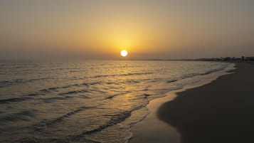 A beach with the sun setting over the water, waves gently lapping at the shore.