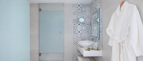 A modern bathroom with a walk-in shower, a large mirror, a white sink, and a white bathrobe hanging on the wall.