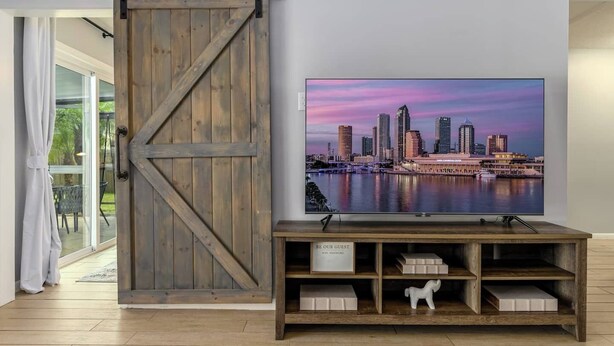 Ein Zimmer mit einer Schiebetür im Scheunenstil, einem Flachbildfernseher auf einem Holzständer und einem Schild mit der Aufschrift 'BE OUR GUEST WITH PASSWORD'.