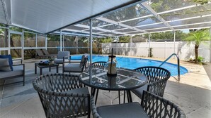 Eine überdachte Terrasse mit Pool, Gartenmöbeln und Blick auf den Garten.