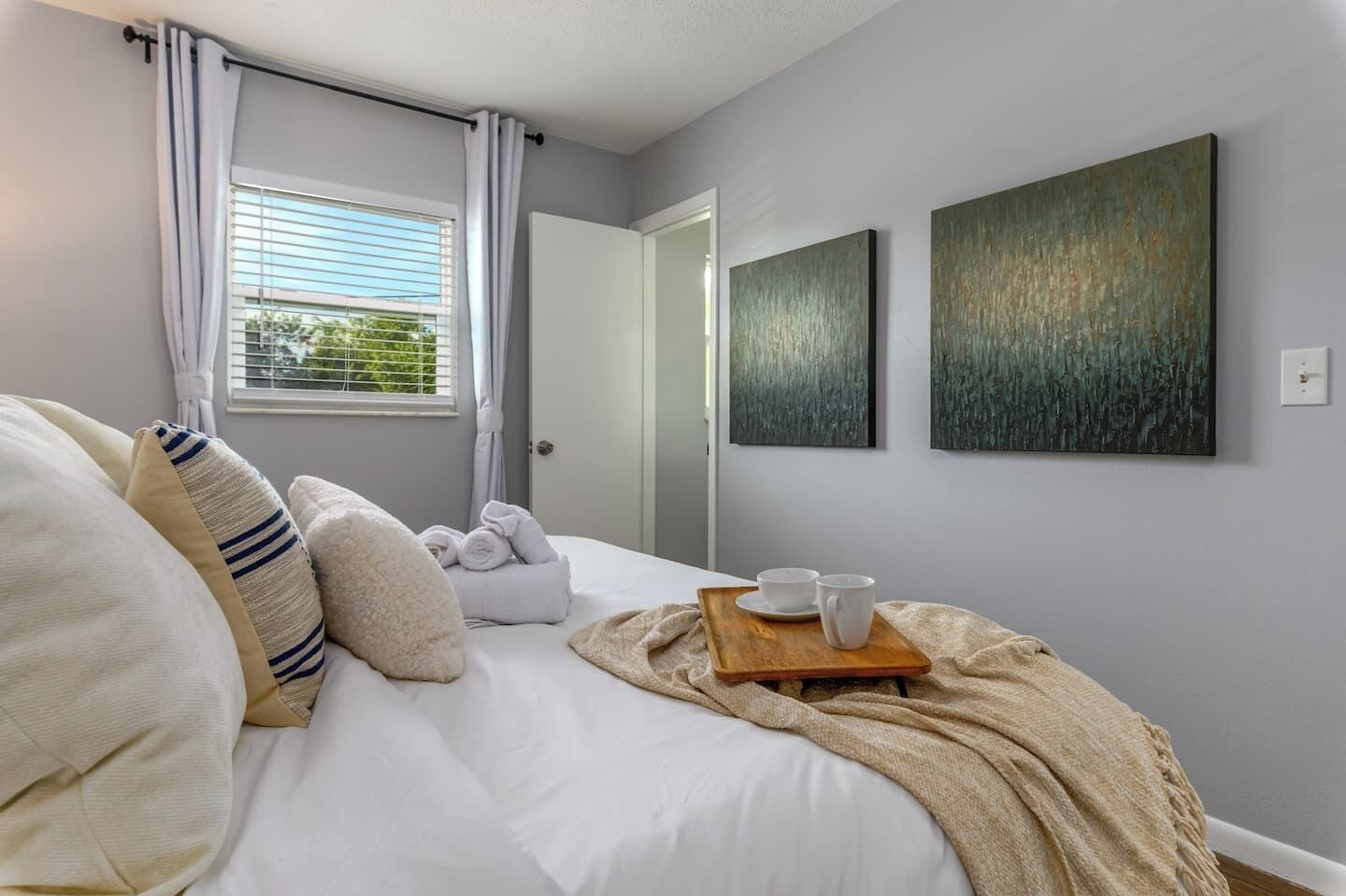 A bedroom with a bed, pillows, a bedside table with cups, and artwork on the wall.