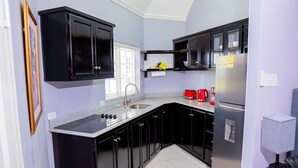 Una cocina moderna con armarios negros, un refrigerador de acero inoxidable, una cafetera roja y una ventana con persianas.