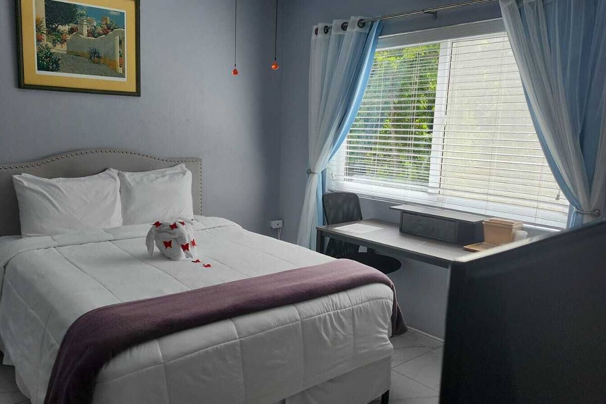 A bedroom with a bed, a desk, and a window with curtains.