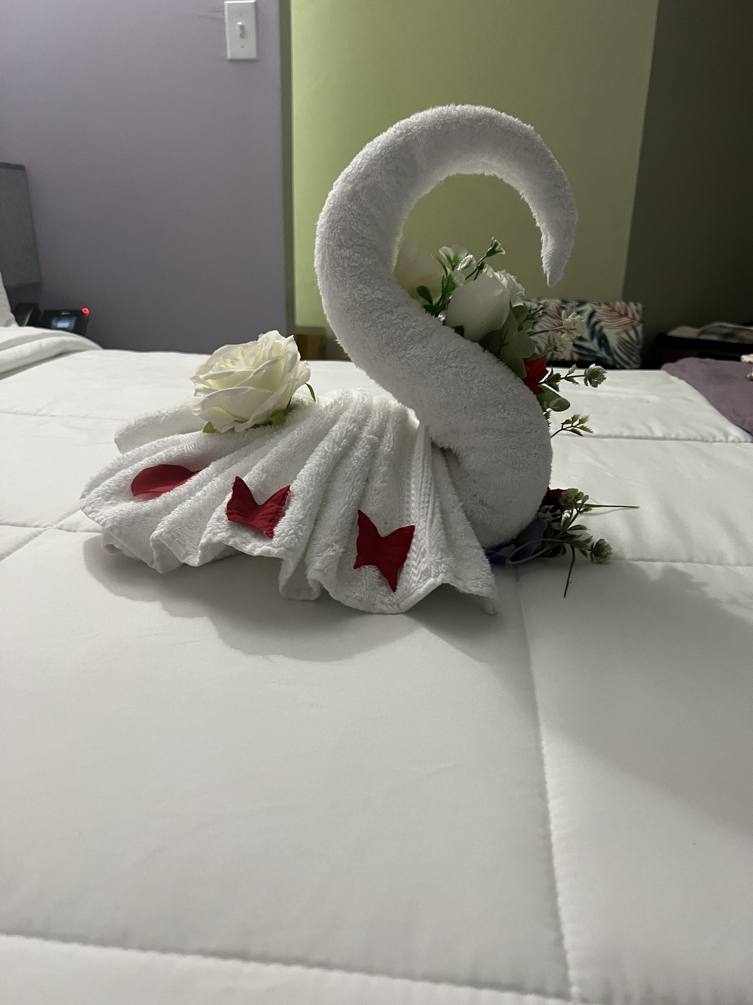 A bed with a swan-shaped towel and a white rose.