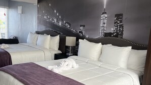 Habitación de hotel con dos camas, ventilador de techo, luz nocturna y un mural con vista a la ciudad.