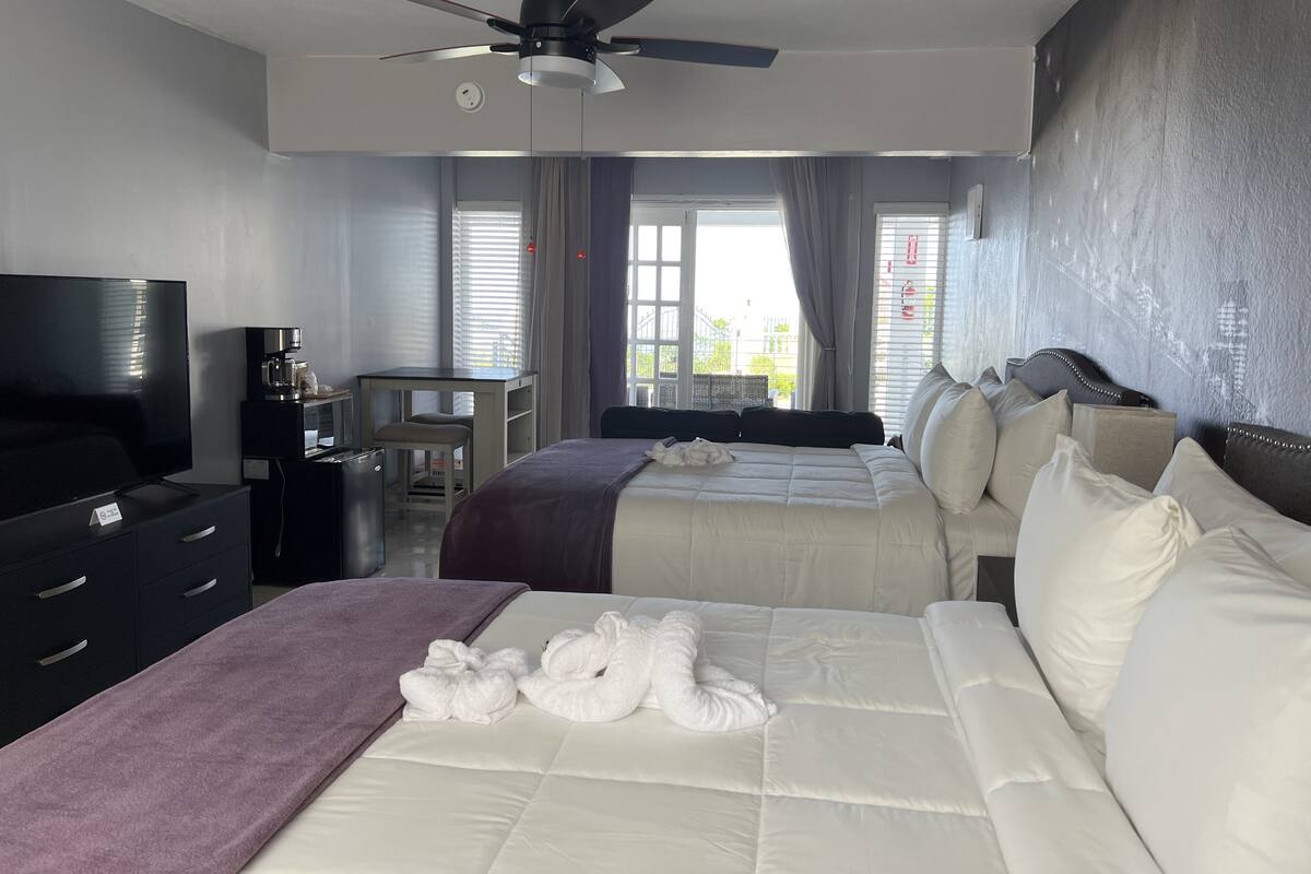 A hotel room with two beds, a TV, a desk with a coffee maker, and a ceiling fan.