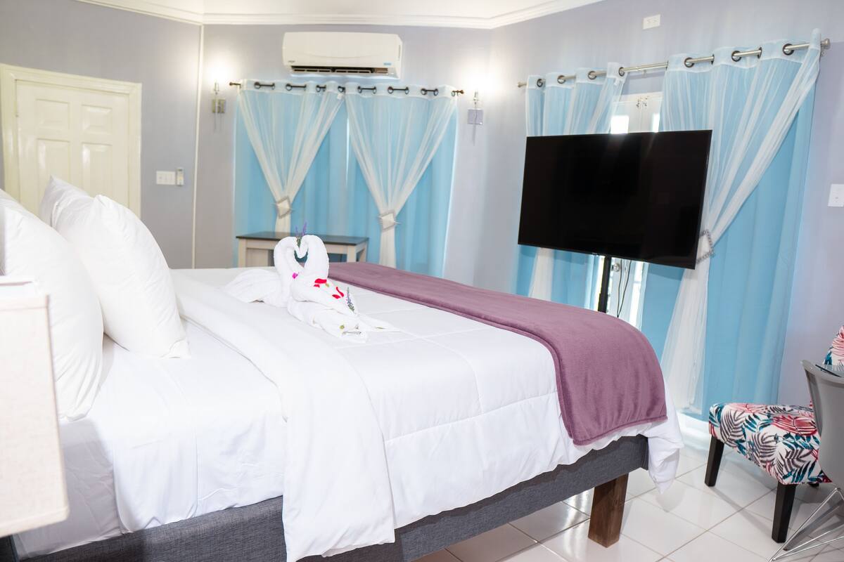A hotel room with a bed, a TV mounted on the wall, a chair, and a desk.