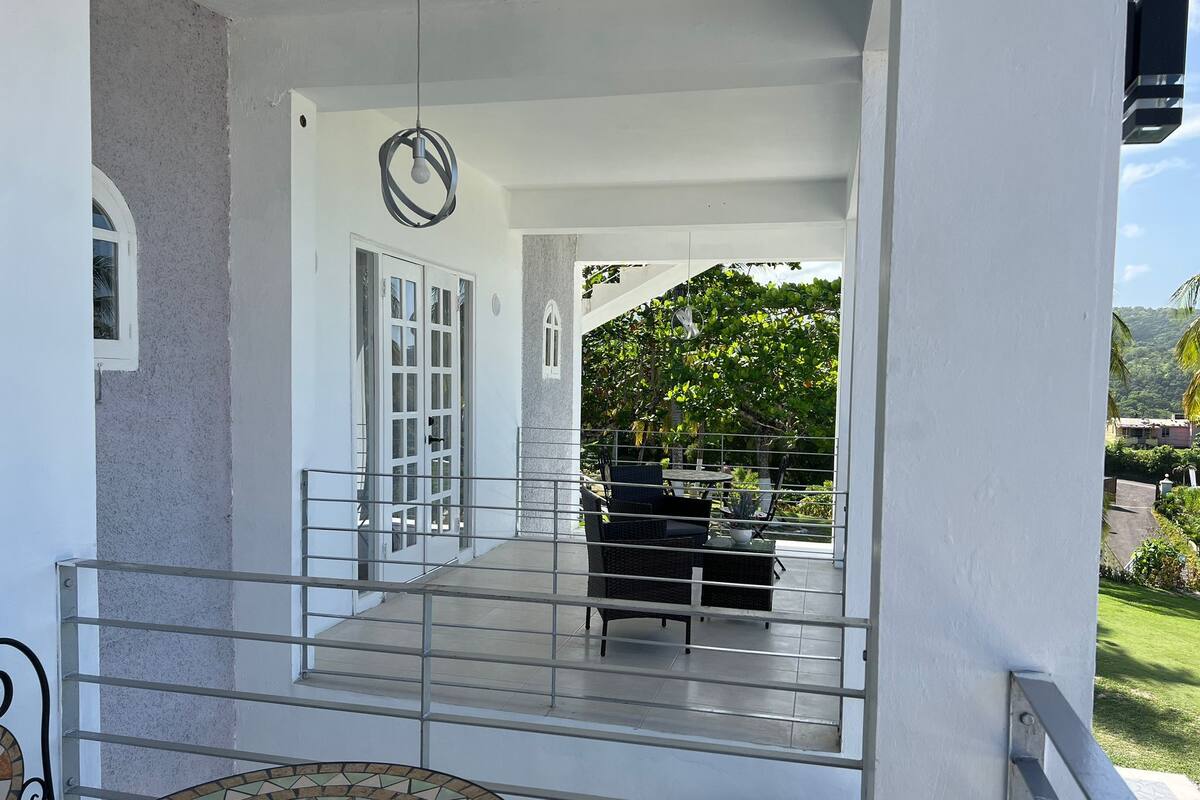 A covered outdoor area with a metal railing, a tiled table, and a seating arrangement.